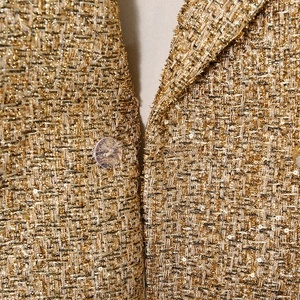 Detailed macro view of woven gold tweed fabric with sequins and clear round buttons