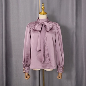 Détail d'un chemisier en satin lilas avec un nœud au col et des boutons dorés chic