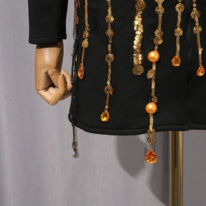 Detail eines schwarzen Kleides mit goldenen Pailletten und orangefarbenen Perlen