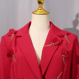 Detail eines roten Blazers mit 3D-Blumenapplikation und goldenen Perlenfransen am Revers