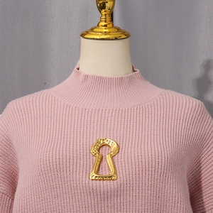 Detail of vintage gold keyhole brooch on pink ribbed knit sweater with textured finish