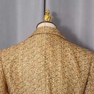 Macro back view of golden tweed blazer jacket showing textured metallic weave on mannequin