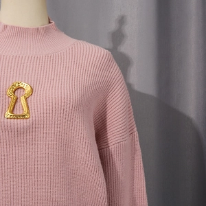 Detail view of pink ribbed knit sweater featuring a unique gold keyhole metal accessory