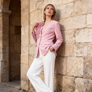 Close-up of pink blazer with 3D floral accent and notched lapels against stone wall