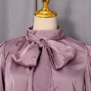Détail d'un chemisier en satin lilas avec un nœud élégant au col et une texture soyeuse