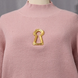 Detailed view of a vintage gold keyhole brooch with hammered texture on a pink sweater