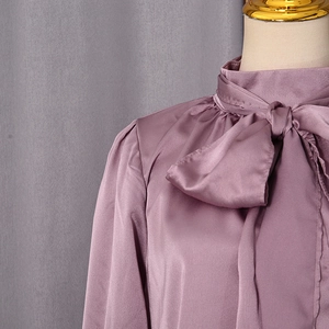 Détail d'un chemisier en satin mauve avec col à nœud papillon et texture soyeuse