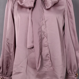 Détail d'un chemisier en satin rose avec grand nœud lavallière et boutons dorés