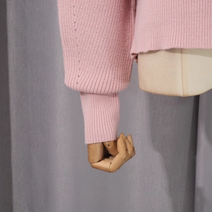 Detailed close-up of soft pink knit sweater with ribbed cuffs on wooden mannequin arm