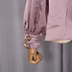 Détail des poignets de chemise en satin rose avec boutons dorés en forme de nœud