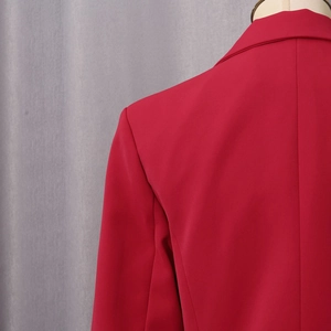 Detail der roten Blazer-Schulternähte und glatten Webstoffstruktur auf grauem Grund
