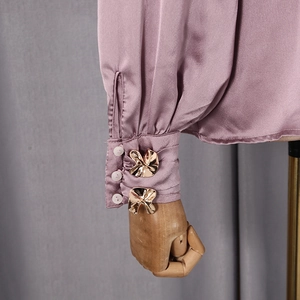 Détail des poignets de chemise en satin rose lotus avec boutons fleurs en métal doré