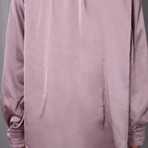 Détail du tissu satiné et des plis aux poignets sur une chemise rose poudré à manches longues