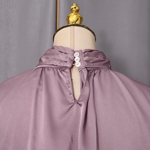 Détail d'un chemisier en satin avec col montant et trois boutons blancs sur l'ouverture dos