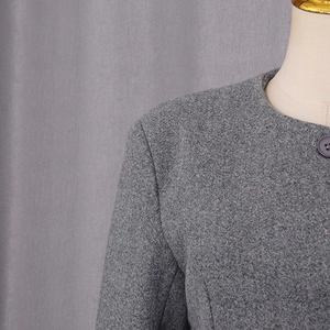 Detailed view of grey wool coat featuring textured tweed fabric and round neckline button