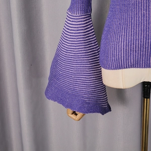 Dettaglio del top in maglia a righe viola con maniche a campana e trama del tessuto