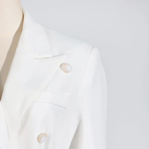 Close-up of white blazer showing peak lapel detail and textured marbled button finish