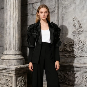 Detail view of dramatic ruffled satin shoulder accents on a black high-fashion blazer