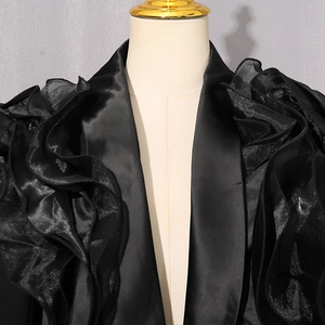Detailed view of layered organza ruffles on black satin blazer jacket with high gloss finish
