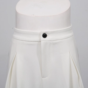 Detail of white wide-leg trousers featuring a single black button and deep waist pleats