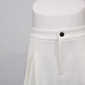 Close-up detail of white wide-leg trousers with black button and pleated design