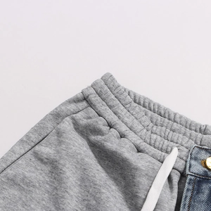 Detail of grey jogger waistband with white drawstring and denim patchwork with gold button