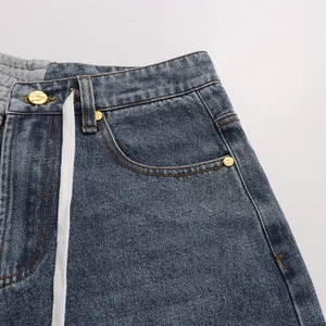 Detail of denim waist with grey sweatshirt patchwork, white drawstring, and gold button
