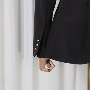 Detail view of black blazer sleeve with golden embossed buttons and textured fabric