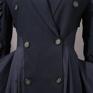 Detail of dark blue double-breasted coat featuring textured buttons and pleated waist