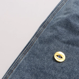 Detail of a golden Evil Eye button accessory on blue patchwork denim jeans fabric
