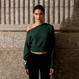Detail of dark green off-shoulder knit sweater with ribbed cuffs and refined texture