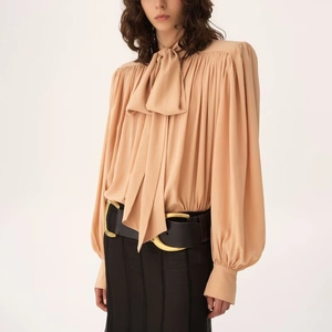 Detail of elegant apricot long sleeve shirt featuring bow-tie neck and pleated lantern sleeves