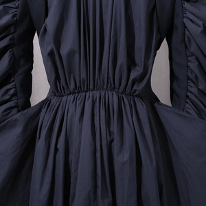 Detail of navy blue coat showing pleated waist design and refined fabric texture