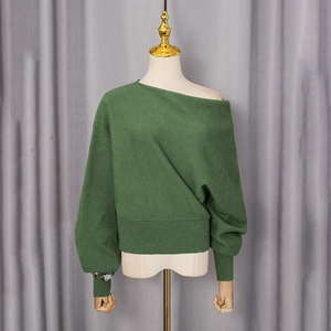 Detail of dark green off-shoulder sweater showing ribbed cuffs and knit texture on mannequin