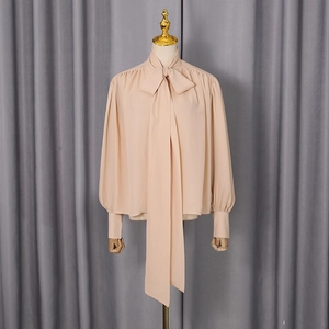 Close-up of elegant apricot long sleeve shirt with large bow tie neckline and pleated cuffs