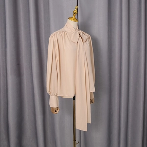 Detail showing the elegant pussy-bow necktie and pleated collar on a beige chiffon blouse