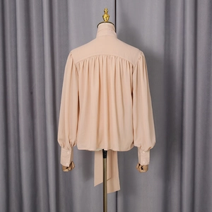 Close-up of beige blouse back with refined pleated details and elegant tie-neck design