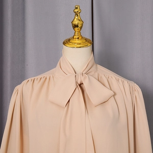 Detail of pussy-bow neckline and pleated shoulders on an elegant apricot chiffon blouse