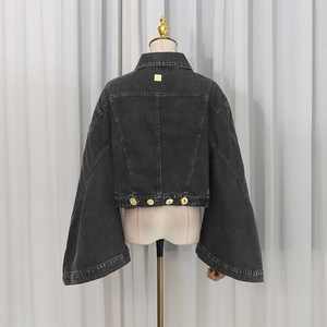 Detailed view of black washed denim jacket featuring golden metal logo and accent buttons