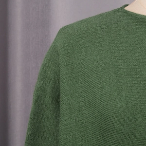 Detail view of dark green knit sweater showing fine texture and neckline craftsmanship