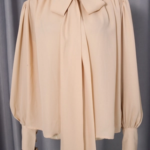 Close-up of elegant beige lantern sleeve shirt with decorative bow and buttoned cuffs