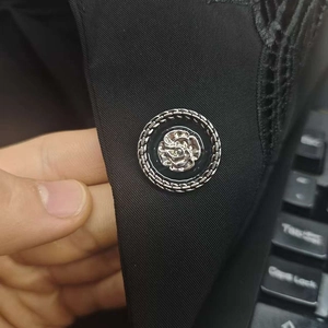 Detail shot of a black blazer featuring an intricate silver rose button with chain borders