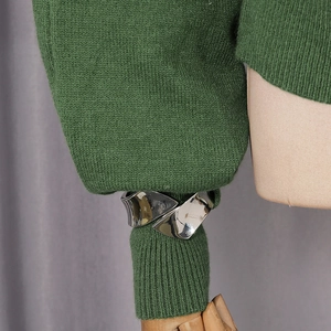 Detail of silver twisted metal cuff bracelet on a knit sleeve with mirror finish