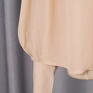 Detailed close-up of pleated cuffs and fine stitching on a beige chiffon blouse