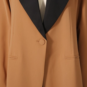 Close-up of color-block blazer with black lapels and caramel fabric with pocket details