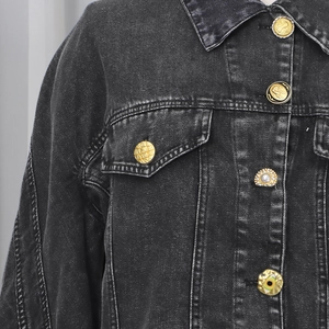 Macro detail of washed black denim jacket featuring unique artistic buttons and rich texture