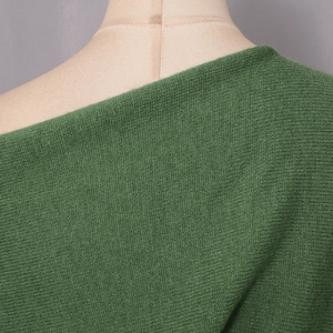 Close-up of dark green off-shoulder knitted sweater showing fine stitch texture