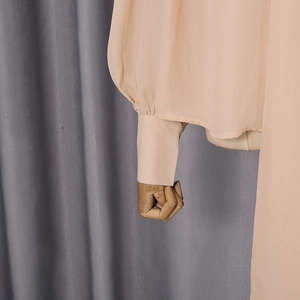Detail view of the buttoned cuff and smooth fabric on the peach long-sleeved shirt