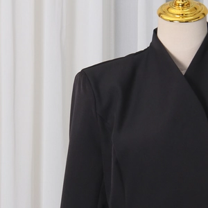 Détail de l'encolure d'une robe blazer noire montrant le tissu lisse et la coupe d'épaule