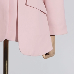 Detail of pink blazer featuring rounded hem, flap pocket, and precise stitching lines